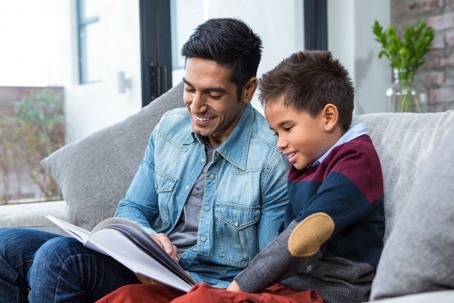 a dad and son reading a book on the couch