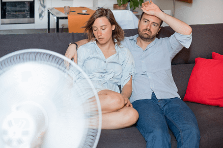a man and woman sitting on the couch with a fan.